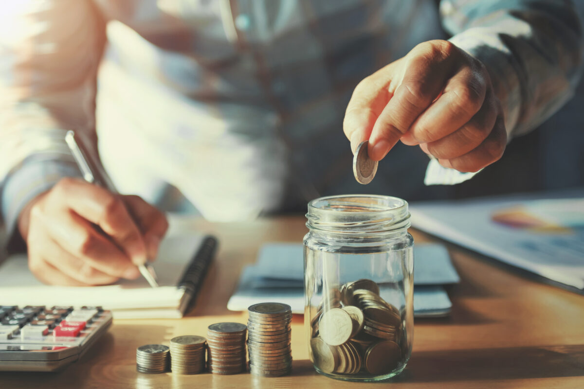 Businessman saving money concept. hand holding coins putting in jug glass