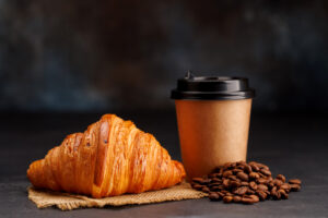 Aromatic coffee in a paper cup paired with a flaky croissant