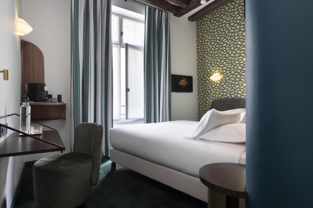 A luxurious and cozy hotel room at Hôtel L de Lutèce, featuring elegant furnishings, a plush bed with fine linens, and large windows offering views of the city.