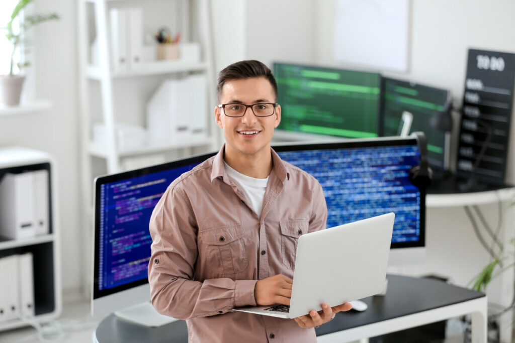 Male programmer holding a laptop and surrounded with computers