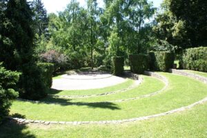 Panoramic view of Parc Watteau, showcasing lush green lawns interspersed with well-maintained walking paths and various tree species, under a clear blue sky.