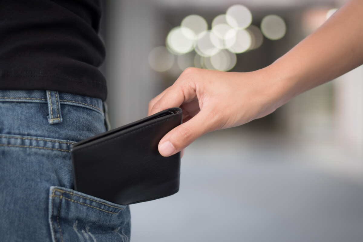 careless woman being pick pocketed; woman facing risk of urban crime of pickpocket or pickpocketing with hand of thief stealing her wallet; urban danger or risk concept; asian young adult women mode