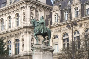 Statue of Étienne Marcel, depicted in medieval garb, standing boldly with a scroll in one hand, located in a busy Parisian square.